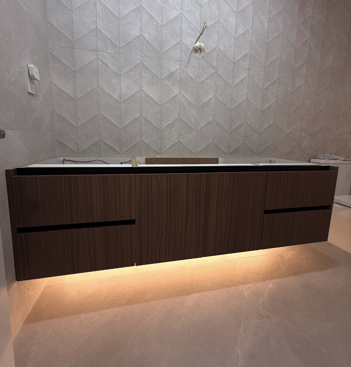 A modern bathroom featuring a floating vanity with integrated lighting, a ceramic accent wall, and large-format floor tile for a clean, contemporary design.