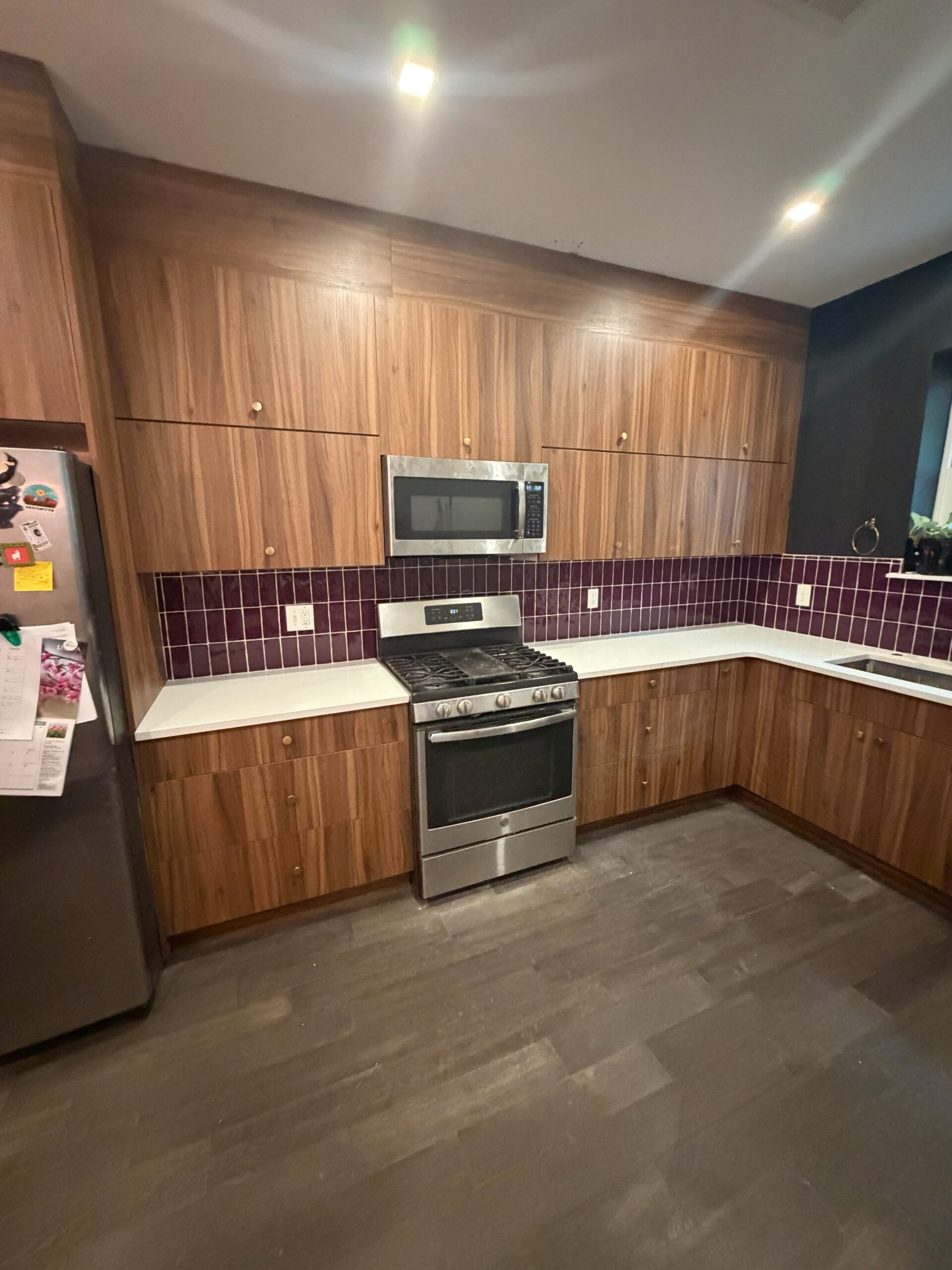 A modern chestnut kitchen with a purple glass backsplash, lift-up cabinets, and quartz countertops, designed for a Philadelphia row house.